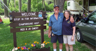 Campground hosts at their host site with sign and camper